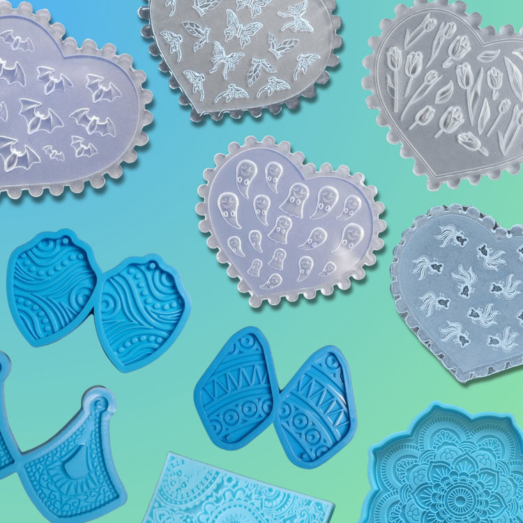 A variety of polymer clay texture and mold sheets featuring heart-shaped plates with embossed patterns of bats, ghosts, butterflies, tulips, and flowing shapes, alongside blue molds with paisley, mandala, and tribal designs.