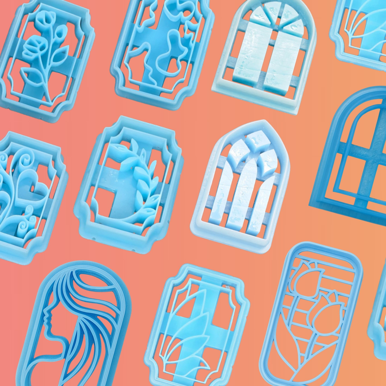 Stained glass-inspired blue polymer clay cutters featuring window frames, floral patterns, hearts, wreaths, and a female silhouette. Arranged on a coral to orange gradient background.
