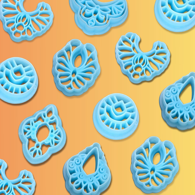 Intricate blue polymer clay cutters with ornate, lacy, and boho-style earring shapes including fans, teardrops, rounds, and florals. Displayed on a soft orange to yellow gradient background.