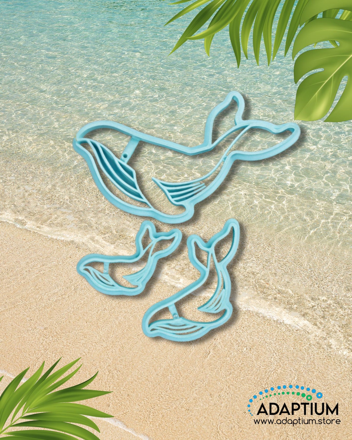 Blue whale polymer clay cutter with smaller whale tail cutters displayed on a beach background with clear turquoise water and tropical leaves.
