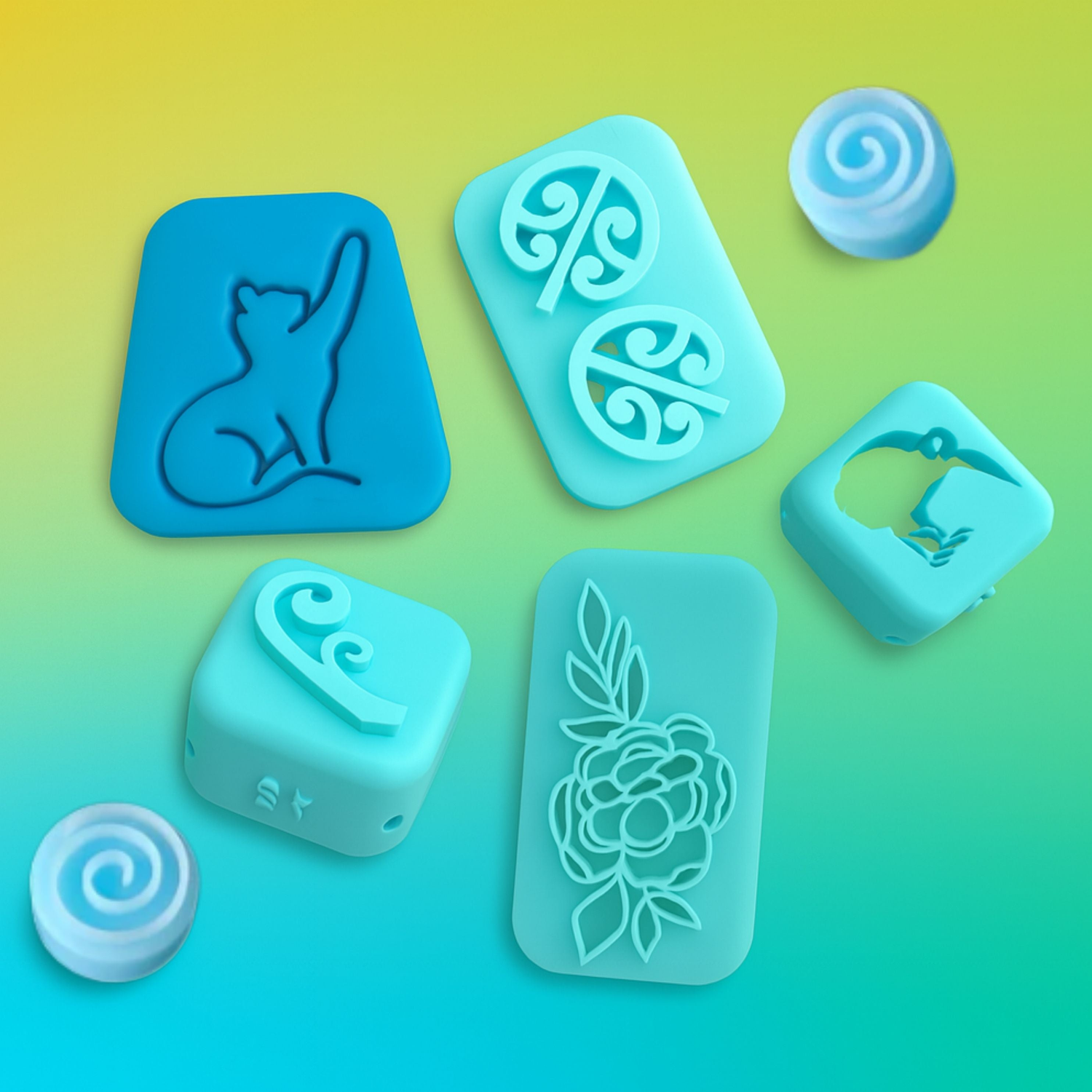 A set of blue polymer clay texture stamps with various designs including a cat, floral patterns, and swirls, arranged on a yellow-to-green gradient background.