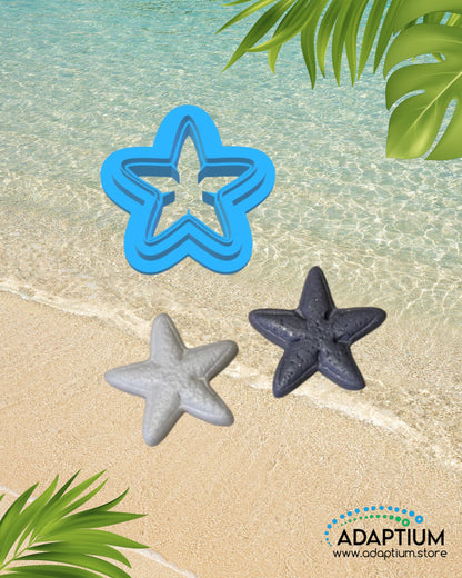 Starfish shaped polymer clay cutter with clay samples colored gray and white placed on sandy beach background with ocean water and tropical leaves.