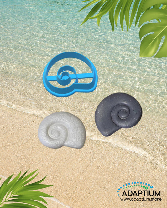 Conch spiral shell shaped polymer clay cutter with two clay samples in colors gray and white placed on sandy beach background with ocean water and tropical leaves.
