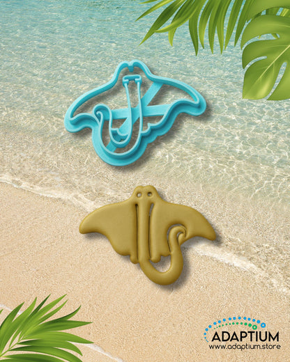 Sting ray polymer clay cutter with matching clay piece placed on a sandy beach background with ocean waves and tropical leaves.