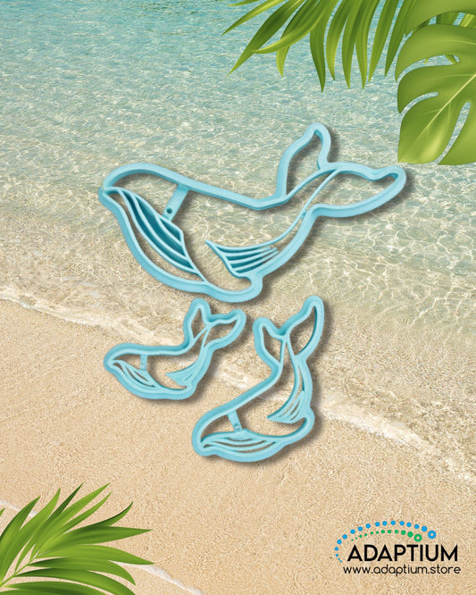 Blue whale polymer clay cutter with smaller whale tail cutters displayed on a beach background with clear turquoise water and tropical leaves.