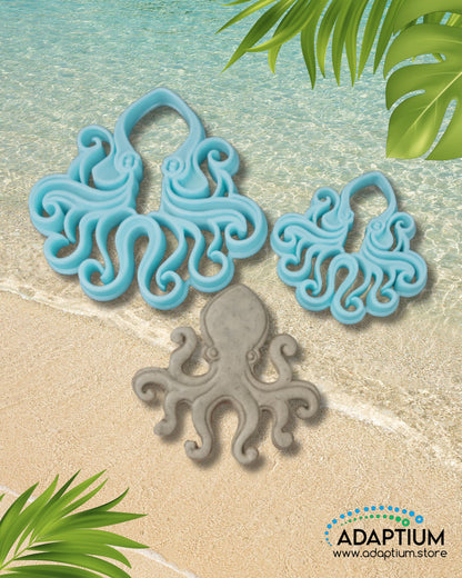 Large and small blue octopus polymer clay cutters with a gray clay octopus piece on sandy beach background with ocean waves and tropical leaves.