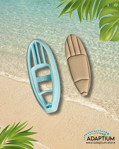 Blue surfboard-shaped polymer clay cutter with matching tan clay surfboard piece displayed on a beach background with tropical leaves.